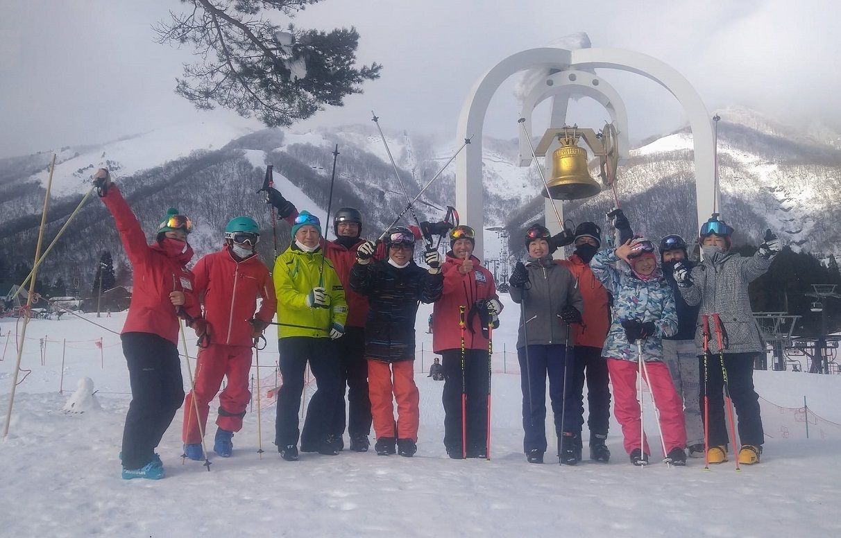 写真　スキーレッスン参加者が鐘の周りに集まって記念写真